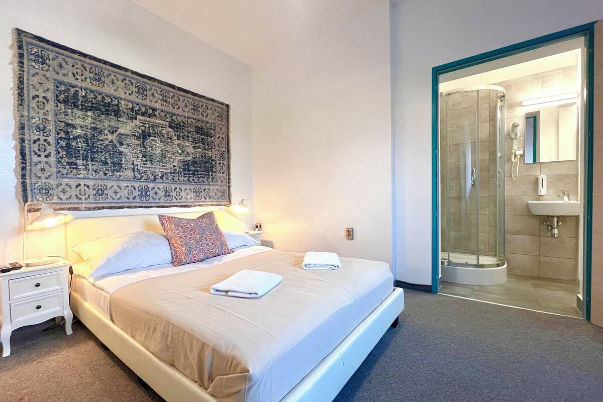 A bedroom with a bed, nightstands, a large patterned tapestry, and a glass-enclosed shower area.