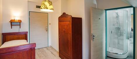 Makuuhuoneessa on puinen sänky, vaatekaappi, ovi ja lasinen suihkuseinä.