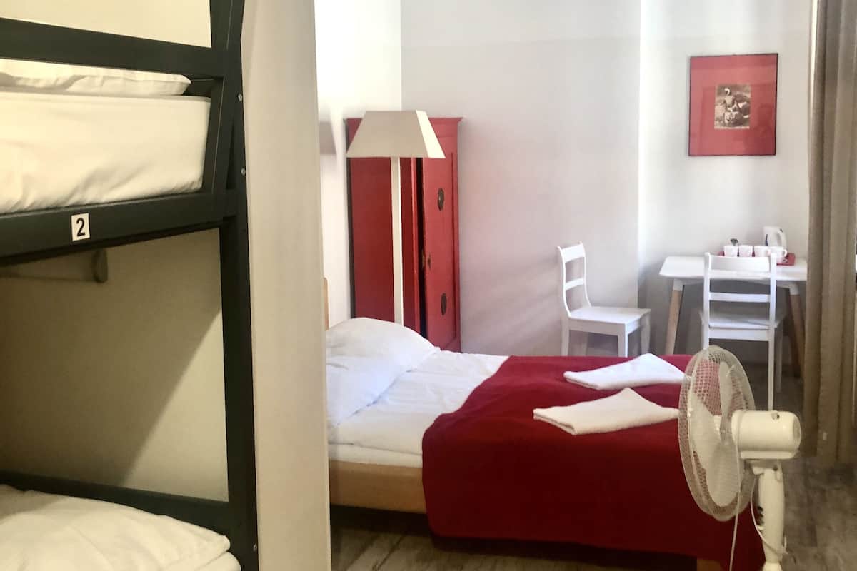 A dormitory room with bunk beds, a desk, a chair, a lamp, and a fan.