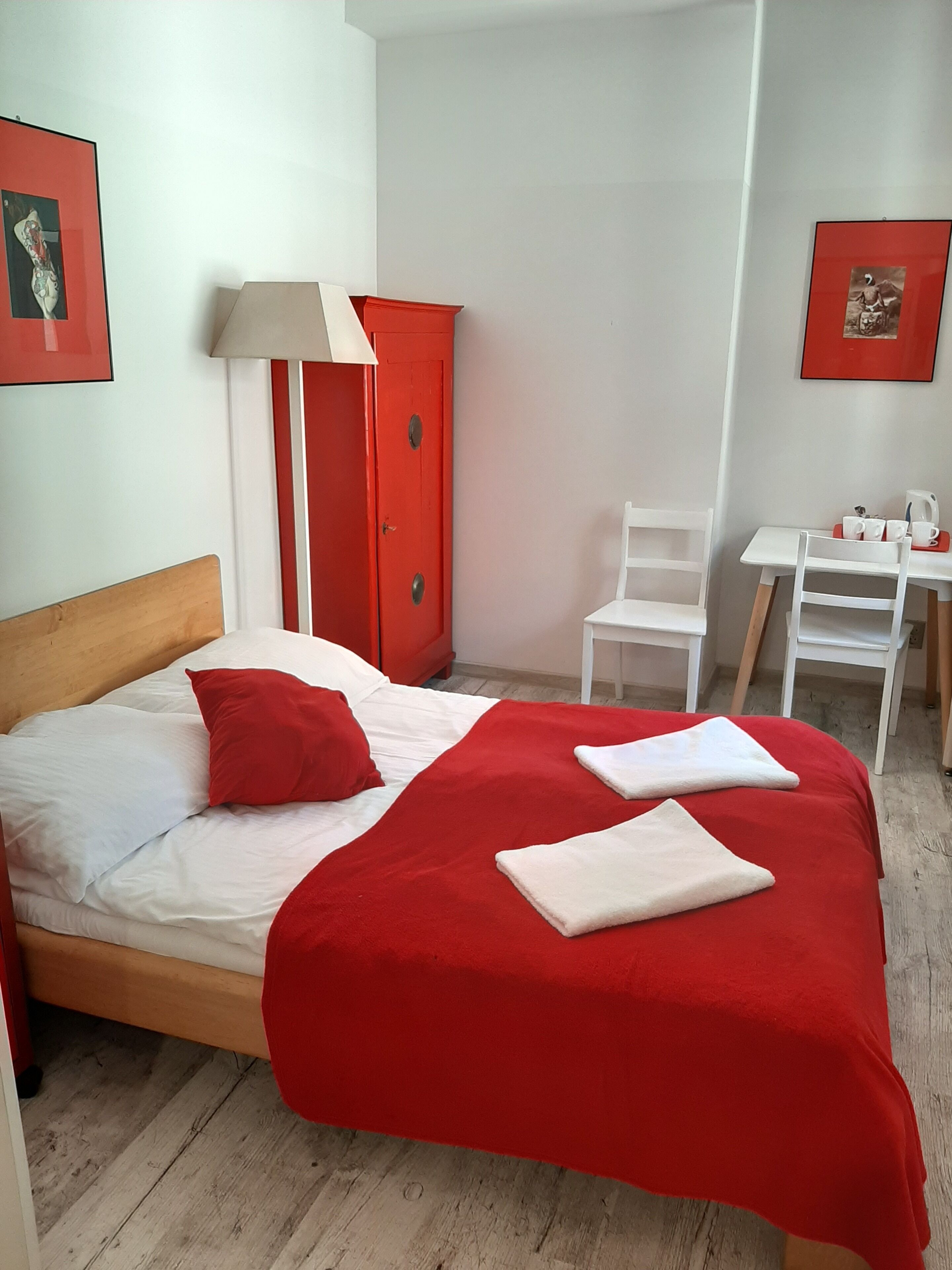 Habitación de hotel con cama, armario rojo, escritorio con silla y mesa con tetera y tazas.