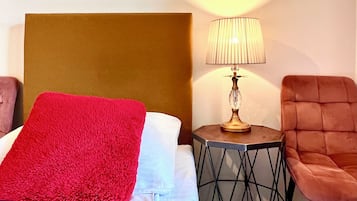 A hotel room with a bed, a red throw blanket, a lamp on a side table, and a chair.
