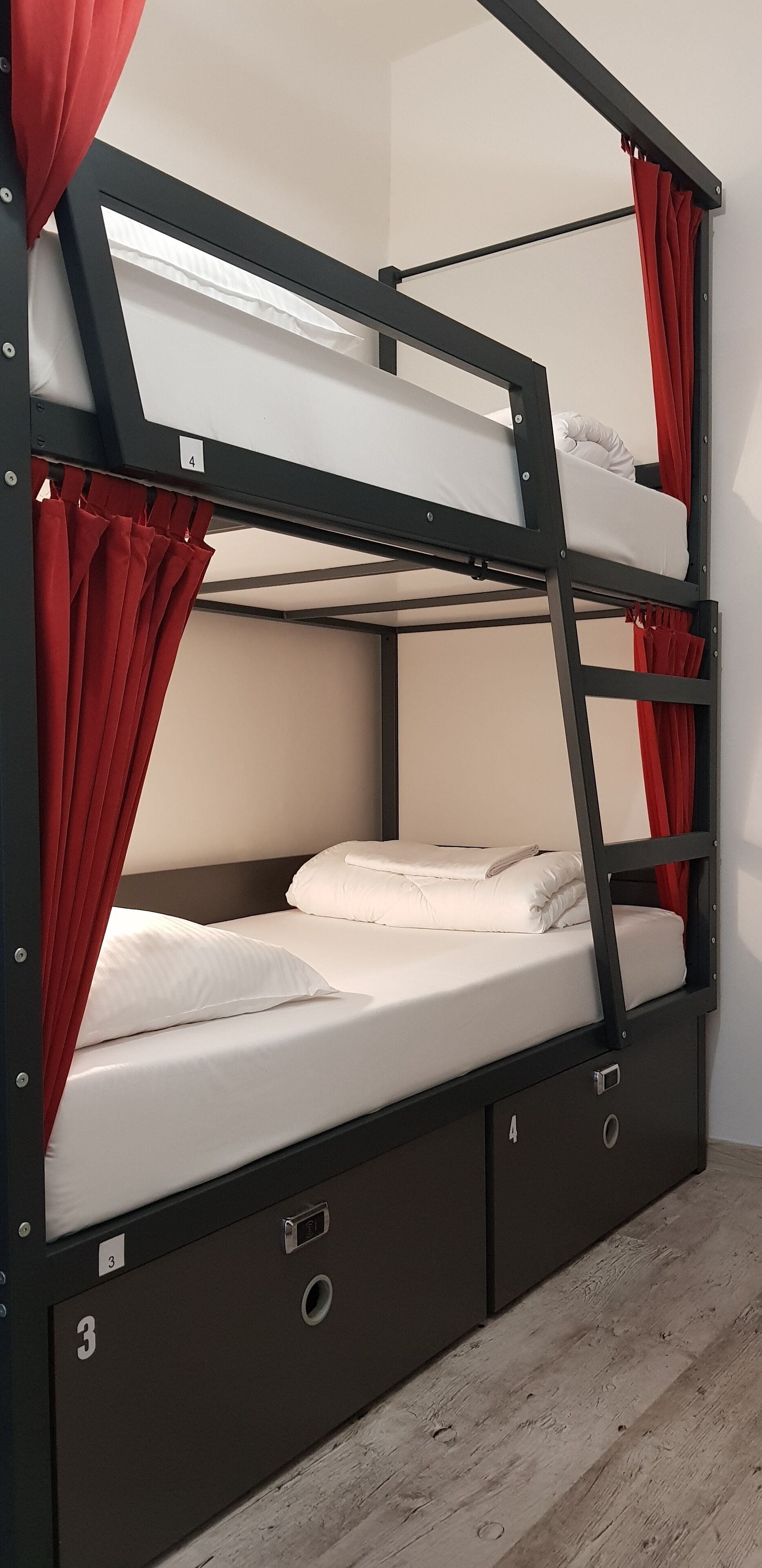 A bunk bed with red curtains, white bedding, and a wooden floor.