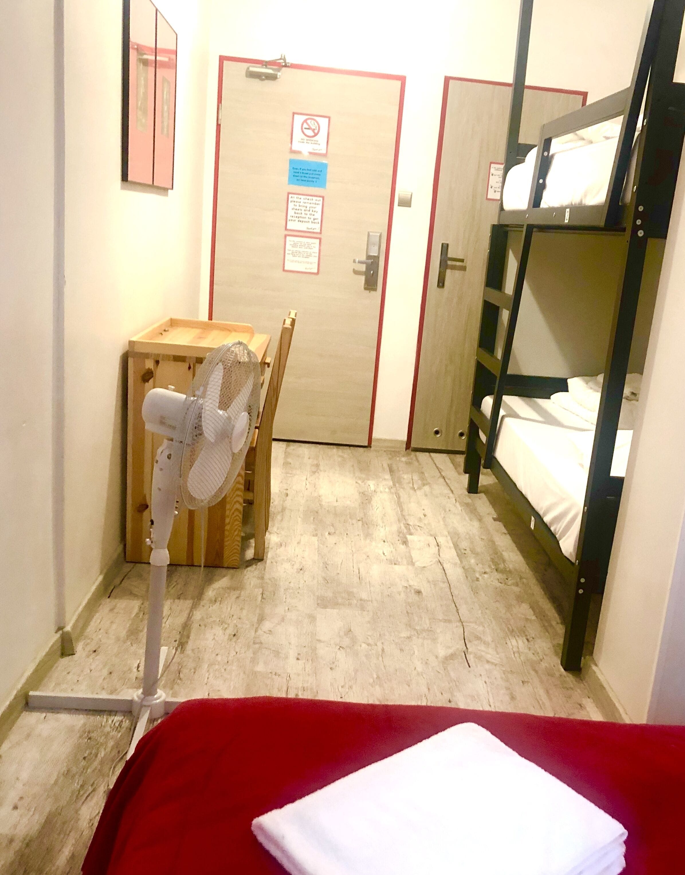 A narrow corridor with a bunk bed on the right, a wooden cabinet with a fan, and a door with a no smoking sign.