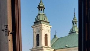 Une vue sur une église à deux tours, surmontée d’un toit végétalisé, que l’on aperçoit à travers une fenêtre.
