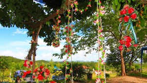 A garden with a swing set, surrounded by trees and flowers. - Baanrai Areeya (Suan Phueng)