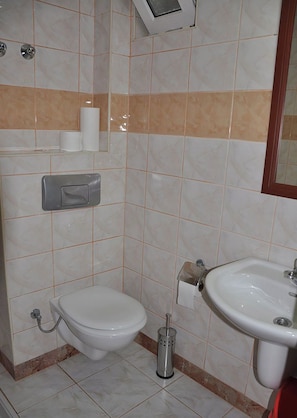 A bathroom with a toilet, a sink, and a towel dispenser. - Tuncer Garden Hotel (Kemer)