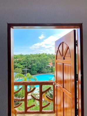 Une porte en bois donnant sur une piscine et une végétation luxuriante.
