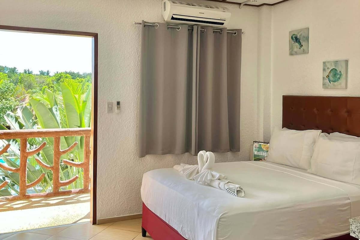 Ein Hotelzimmer mit Bett, Klimaanlage, Blick auf Grünflächen und einem Balkon.