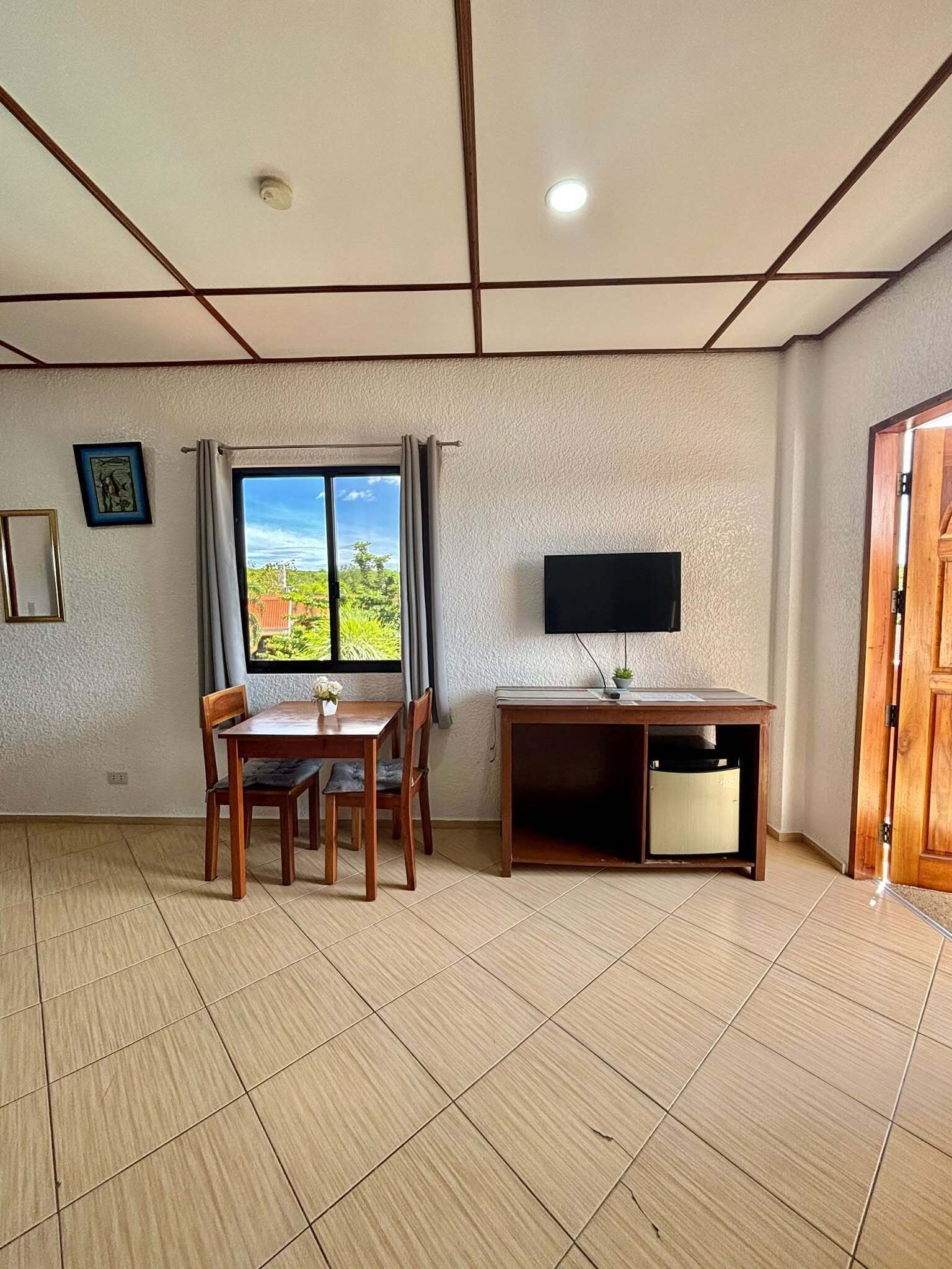 A room with a dining table, chairs, a TV, and a window with curtains.