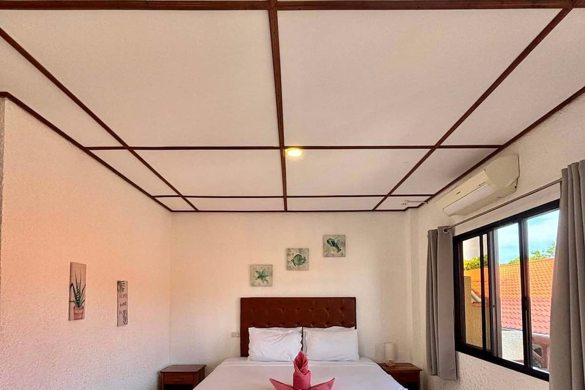 Ein Hotelzimmer mit einem Bett, einem Nachttisch, einem Fenster mit Vorhängen und einer Decke mit Rastermuster.