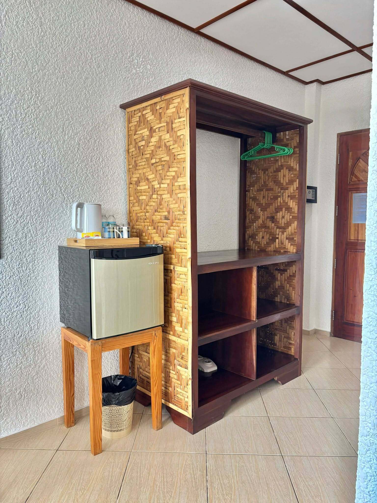 Una habitación con un armario de madera, un taburete pequeño y una prenda verde colgada de un perchero.