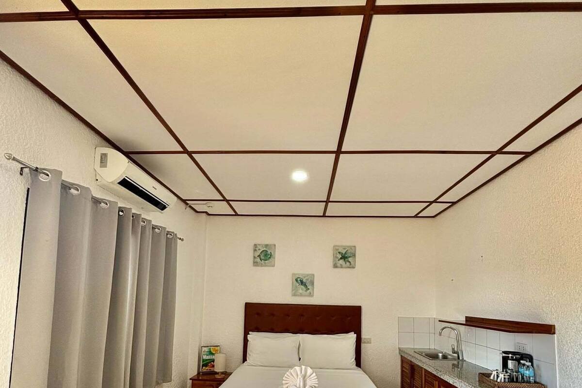 Ein Hotelzimmer mit Bett, einer kleinen Küchenzeile, einem Badezimmer und einer Decke mit Rastermuster.
