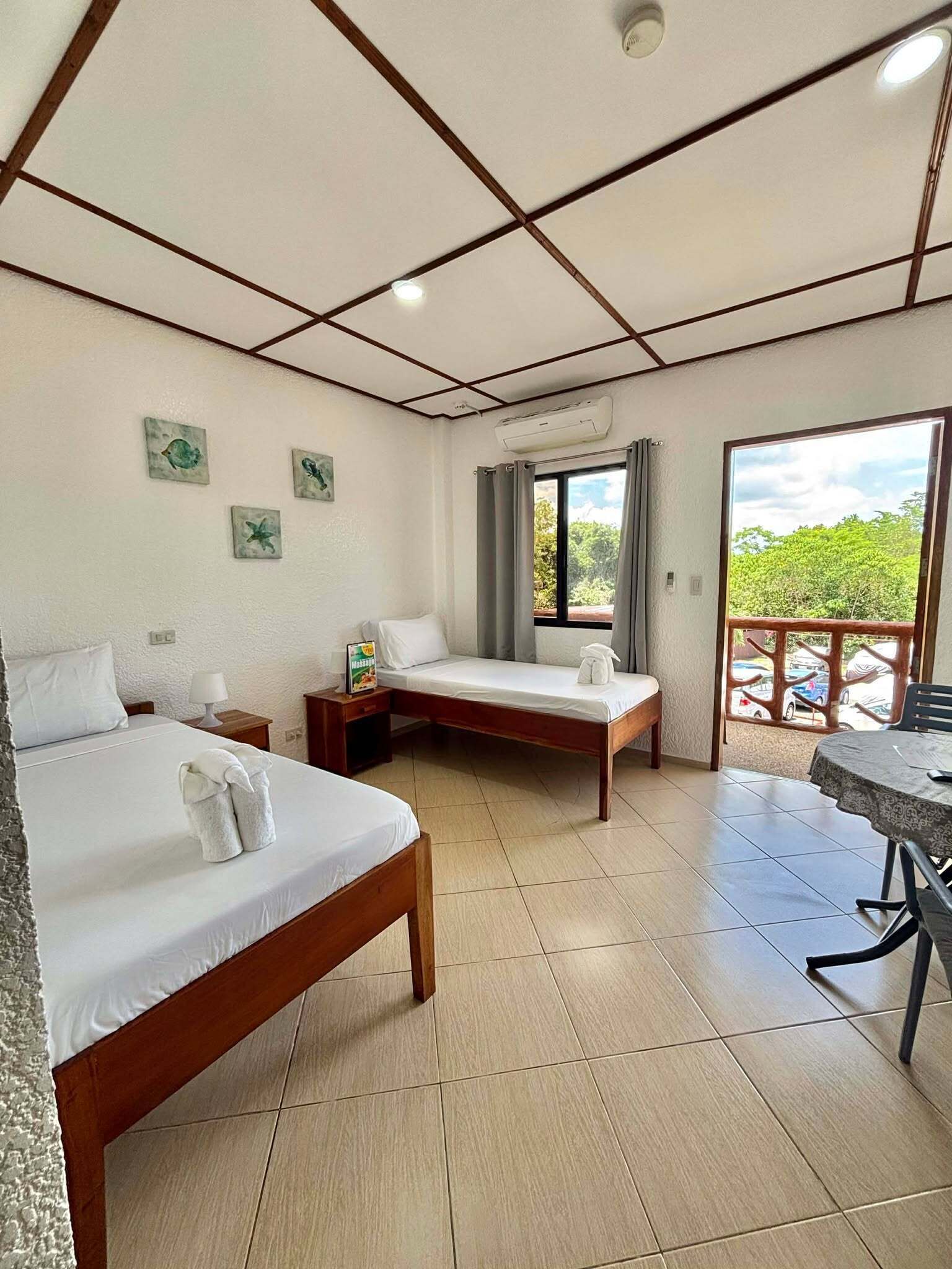 A hotel room with two beds, a small table, and a balcony with a view.