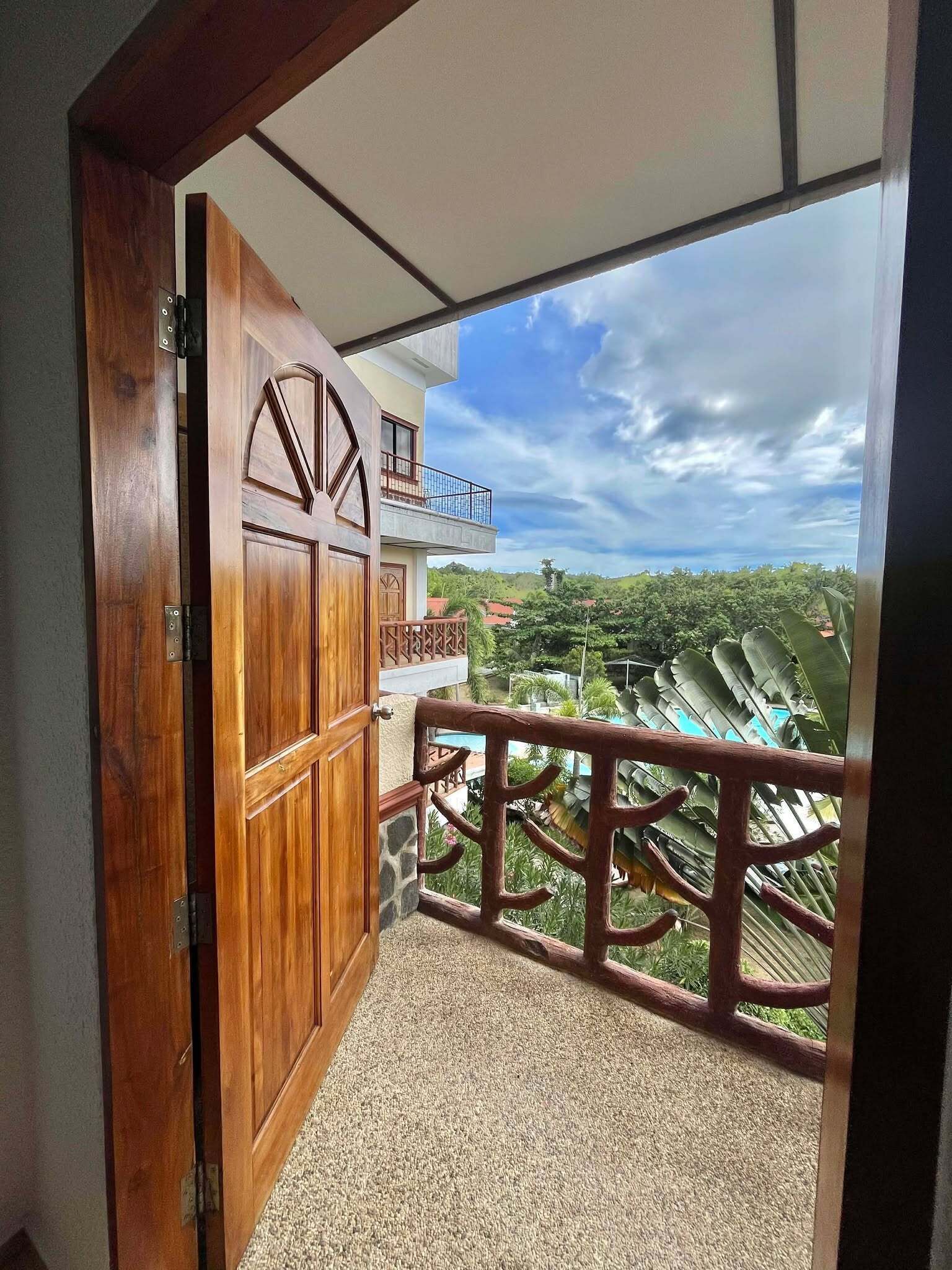 A wooden door leading to a balcony with a view of a residential area and a clear sky.
