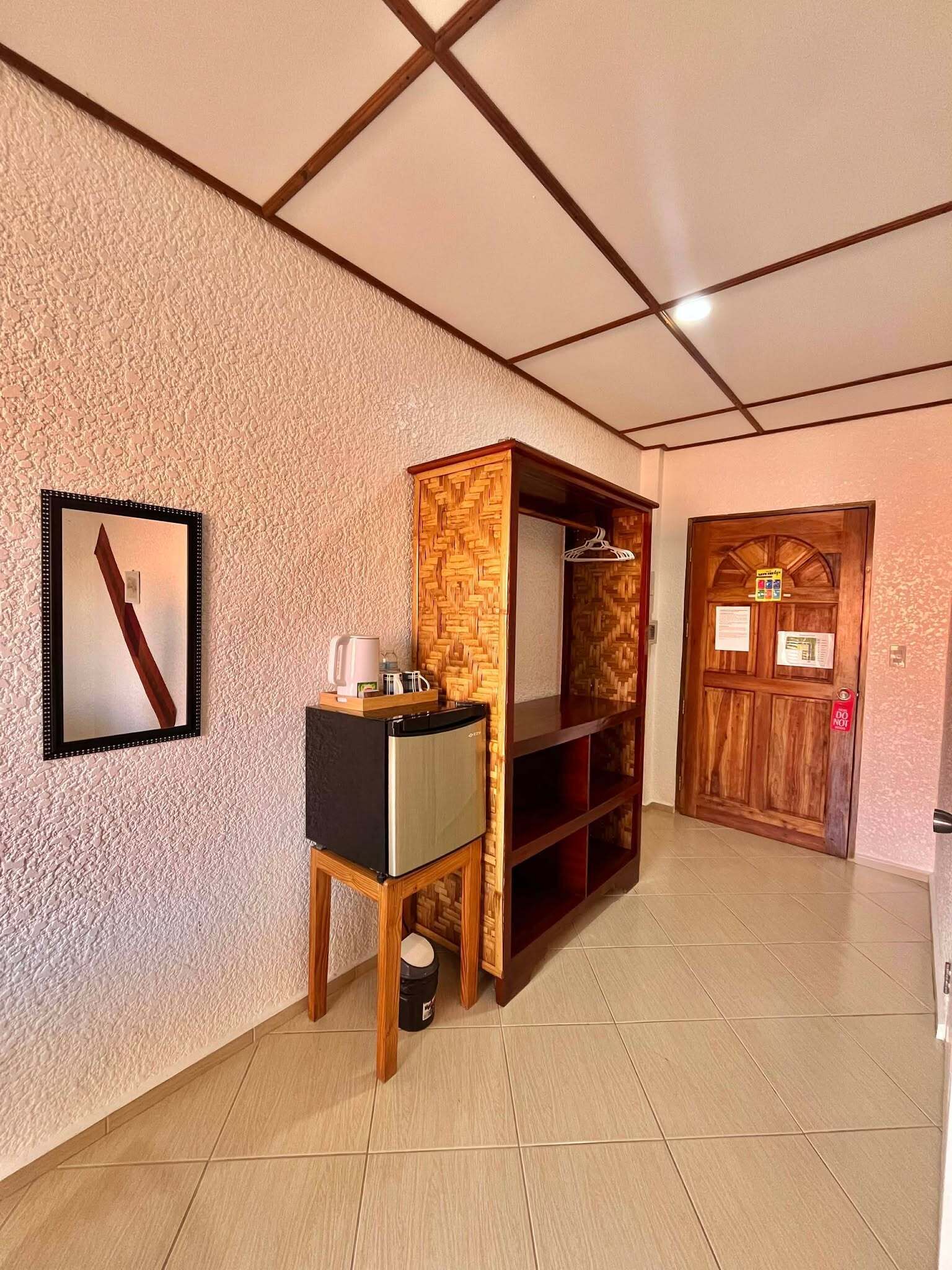 A room with a textured wall, a framed picture, a wooden cabinet, a small table with a kettle, and a door with a 'Do Not Enter' sign.