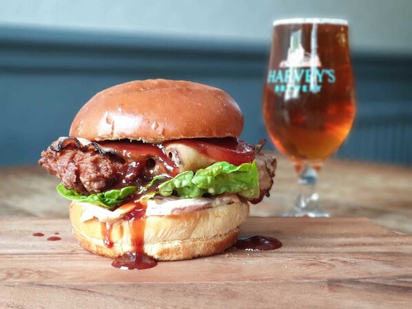 A burger with lettuce, cheese, and sauce, and a glass of beer on a wooden table.