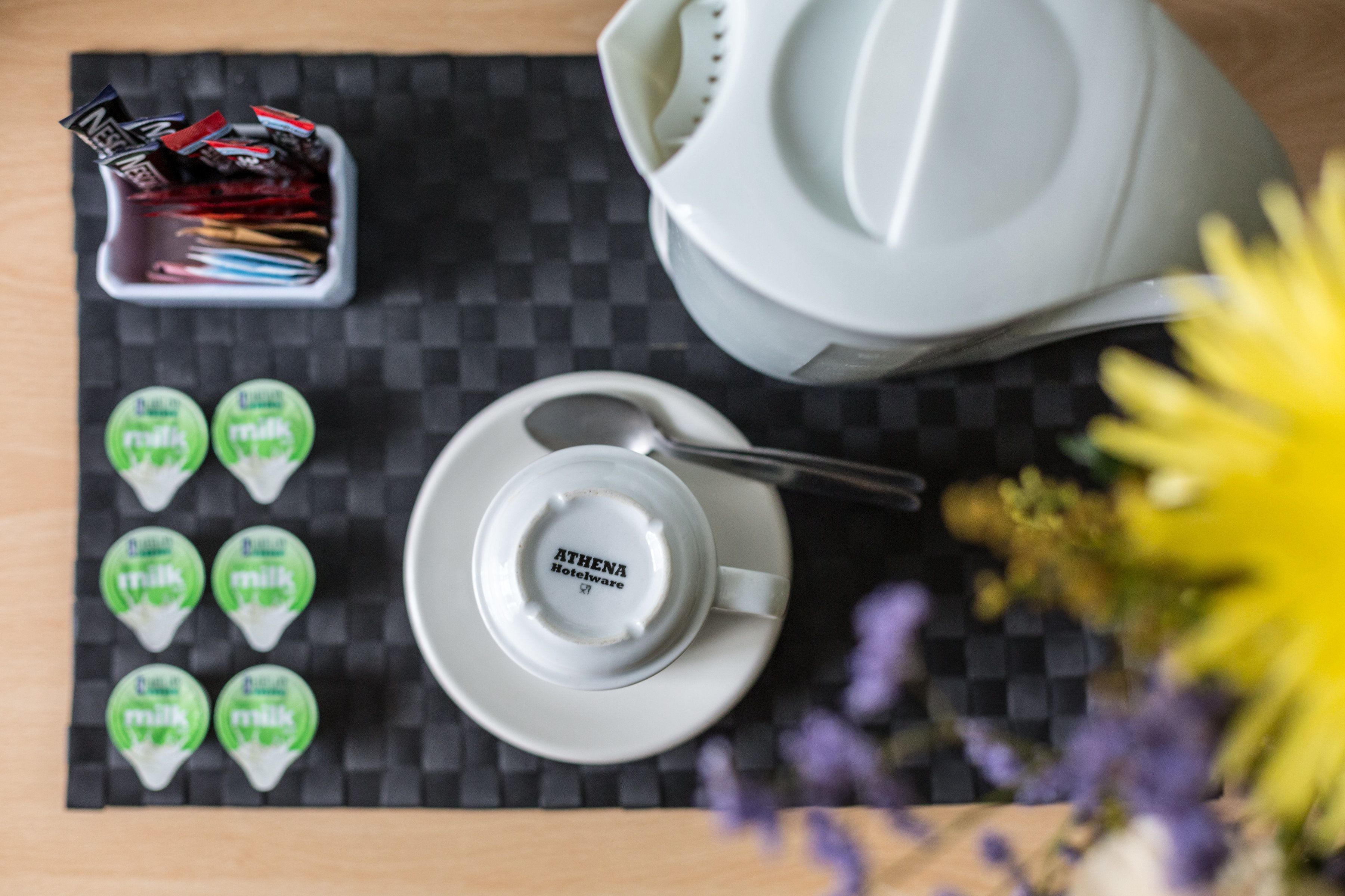 A table with a coffee pot, a cup and saucer, a mug, a container of coffee stirrers, and six packets of milk.
