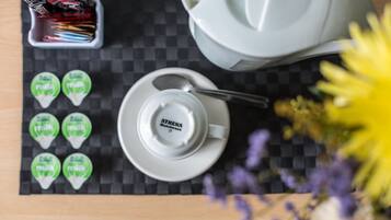A table with a coffee pot, a cup and saucer, a mug, a container of coffee stirrers, and six packets of milk.
