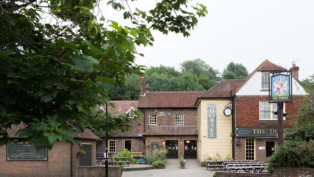 A traditional pub with a sign reading "The Dorset" and a clock above the door. - The Dorset (Lewes)