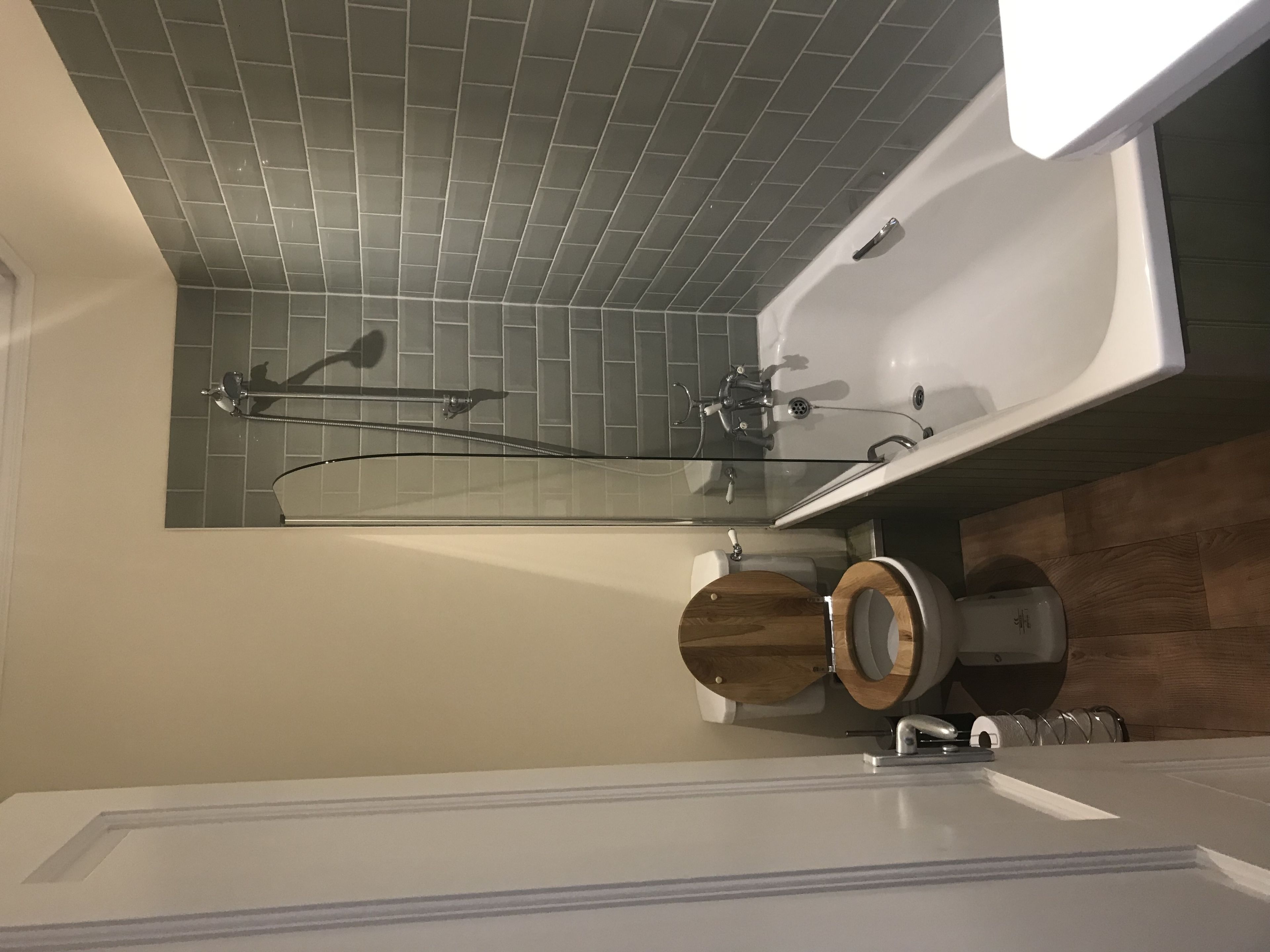 Un bany modern amb dutxa de vidre, vàter de fusta i banyera blanca.