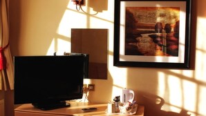 A hotel room with a television, a framed picture on the wall, a lamp, and a small table with a remote control, a cup, and a tissue box. - The Dorset (Lewes)