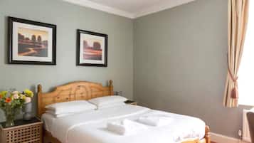 Una cama bien hecha en una habitación con cabecera de madera, dos cuadros enmarcados en la pared y una ventana con cortinas.