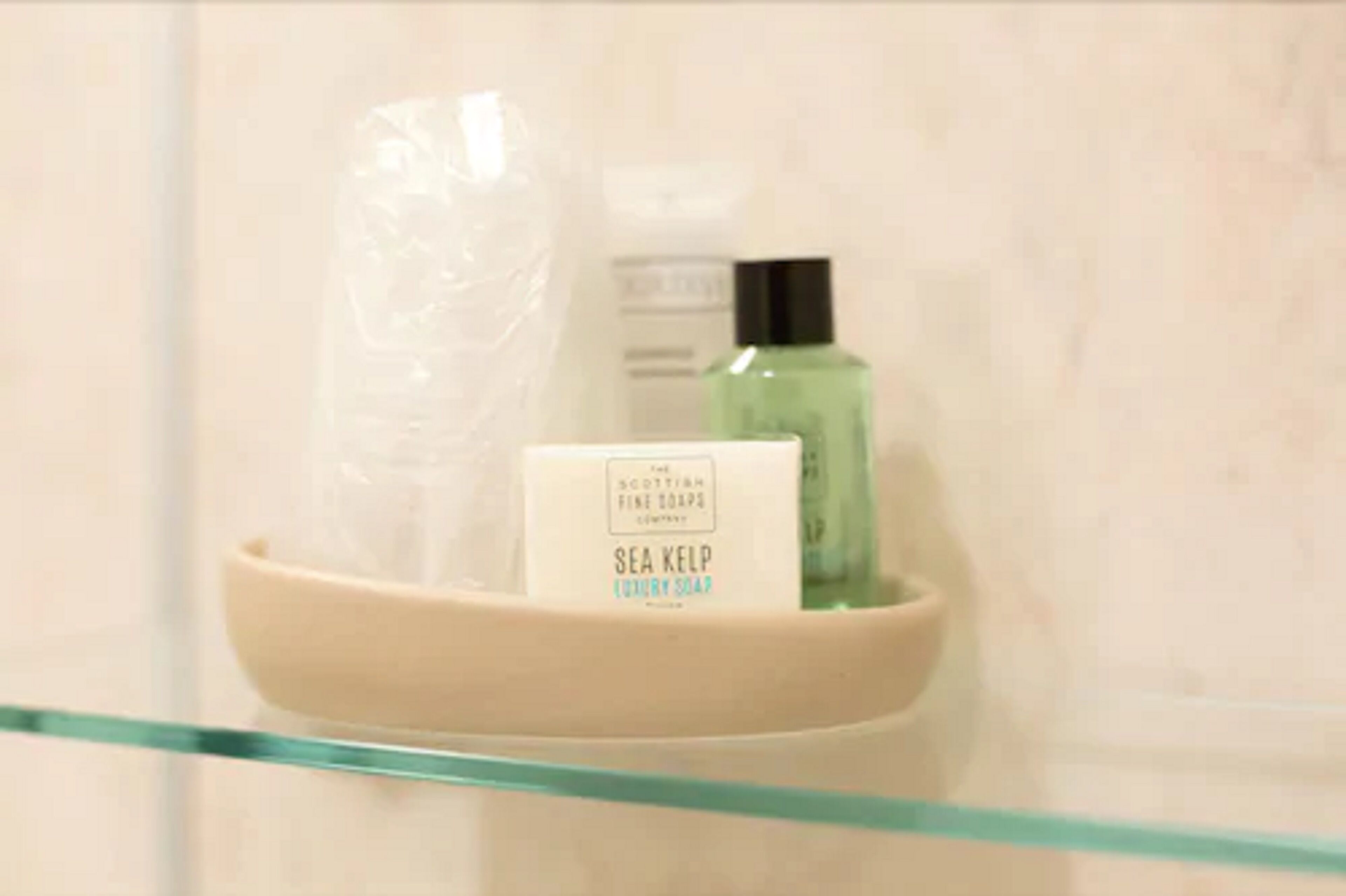 Un baño con un estante de vidrio que contiene una botella blanca con la etiqueta 'Sea Kelp Luxury Soap' y una botella verde.