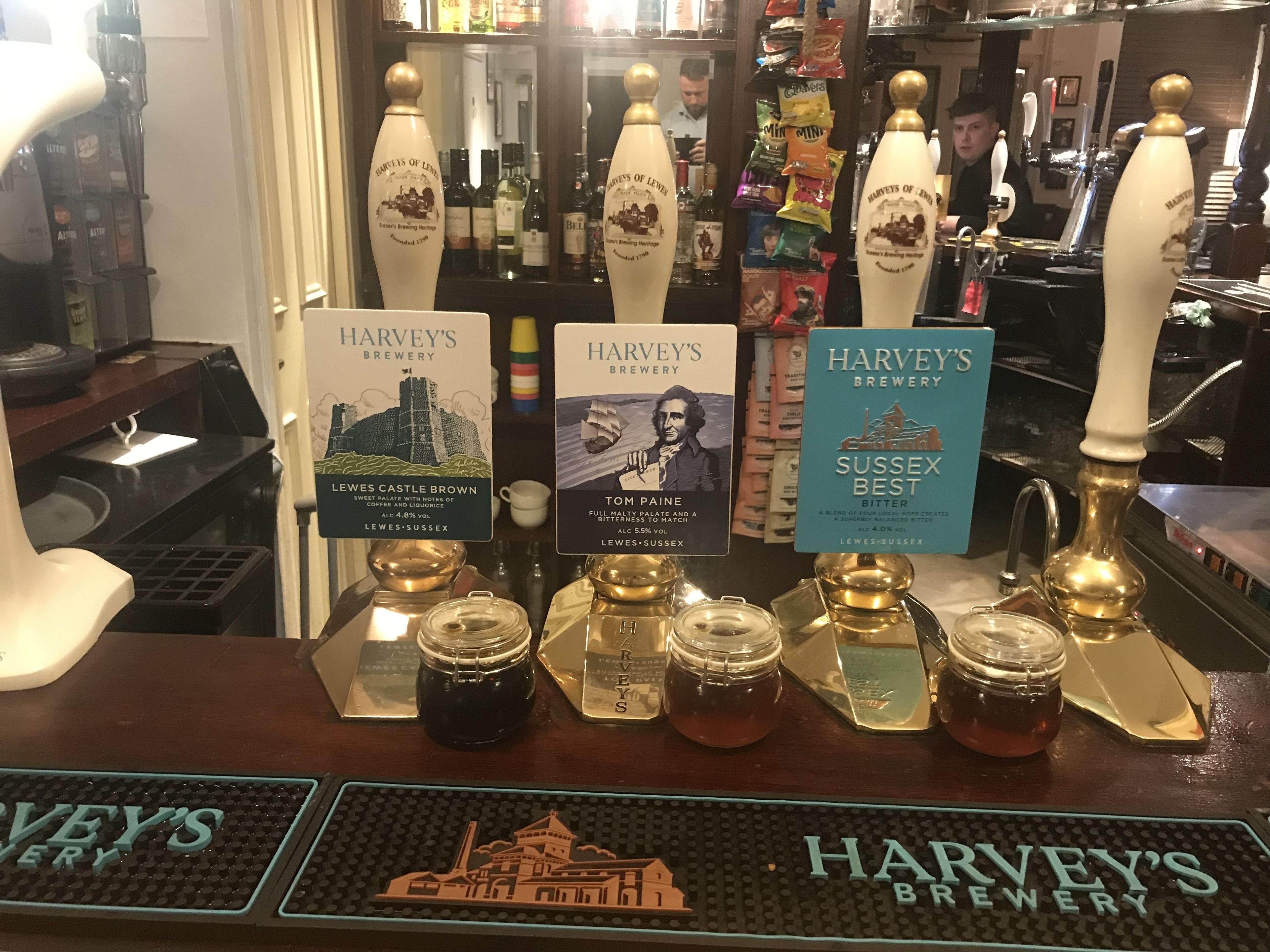 A bar area with multiple taps labeled with different beer names and a selection of jars.