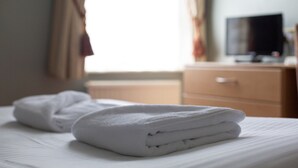 A neatly made bed with folded white towels and a television on a wooden dresser in the background. - The Dorset (Lewes)