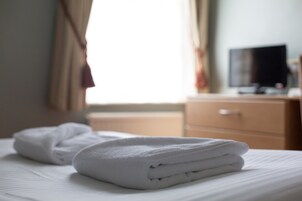 Cama bem arrumada com toalhas brancas dobradas e uma televisão em um aparador de madeira ao fundo.