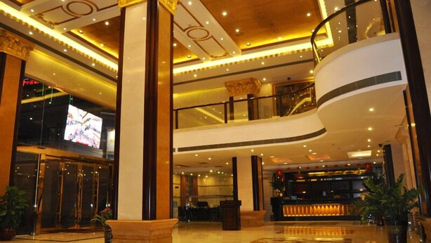 A multi-level hotel lobby with a grand staircase, a reception desk, and a large screen displaying a sports event. - Golden Island Holiday Hotel Foshan (Foshan)