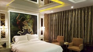 A hotel room with a large bed, two armchairs, a small table, and a painting of a woman on a swing. - Golden Island Holiday Hotel Foshan (Foshan)