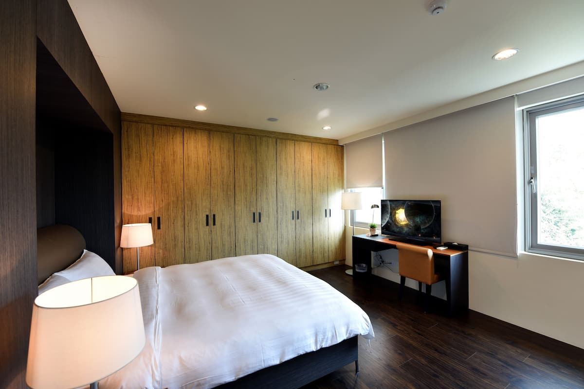 A modern hotel room with a large bed, a desk with a television, and a wardrobe.
