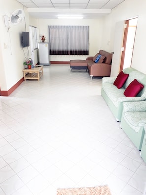 A living room with a sofa, a coffee table, a TV, and a fan.