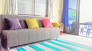 Una habitación con sofá, almohadones de colores, alfombra a rayas y vista al exterior a través de un ventanal.