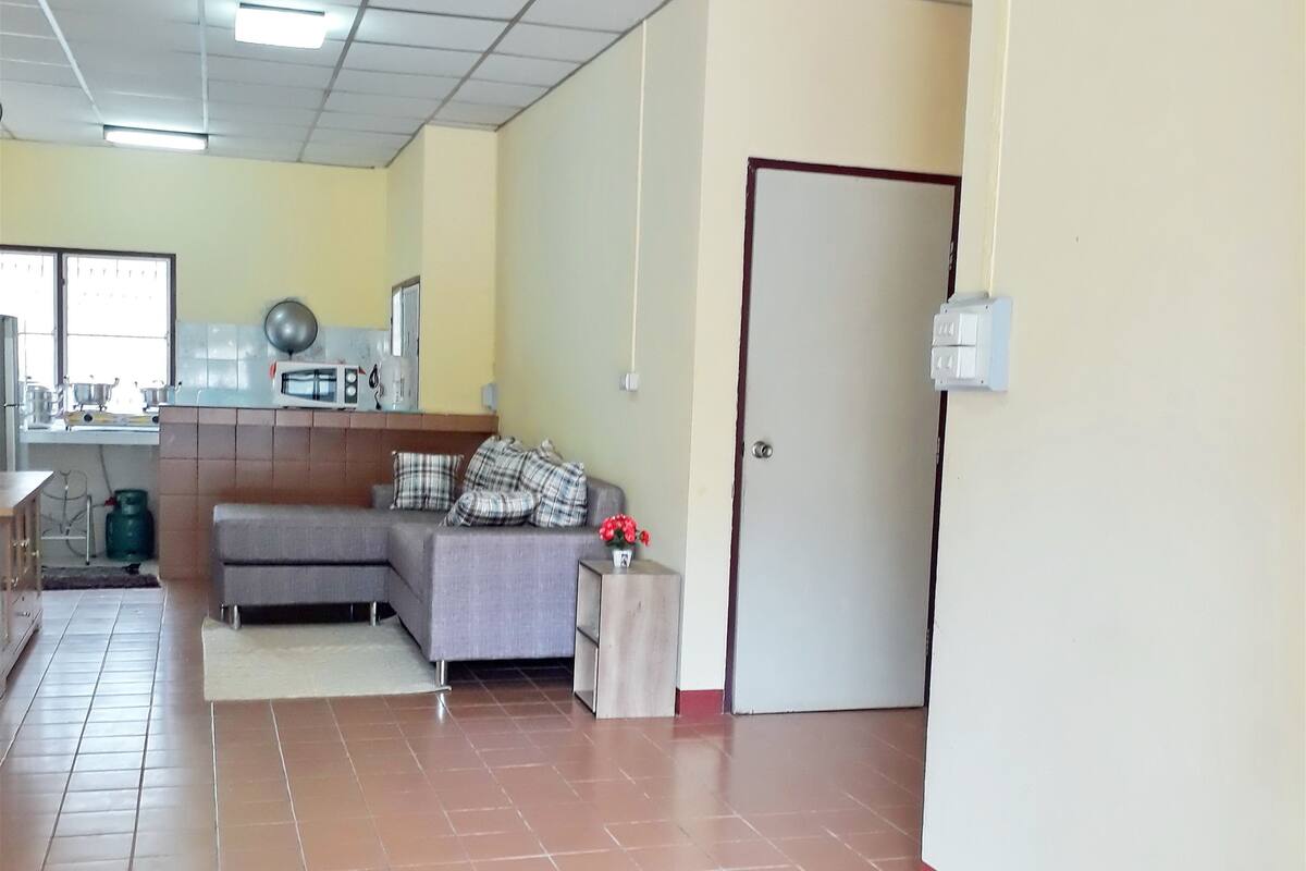 Una habitación amplia con suelo de baldosas, un sofá, una mesita con un jarrón y una puerta.