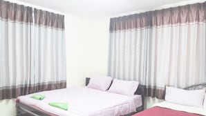 Habitación de hotel con dos camas, una con cubrecama rosa y la otra con cubrecama roja. Ambas camas tienen almohadas y toallas dobladas. La habitación tiene cortinas en las ventanas.
