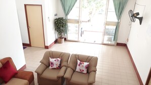 Una sala de estar con dos sofás, una mesa de centro con un centro de flores, una planta en maceta y un ventanal corredizo que da al exterior.