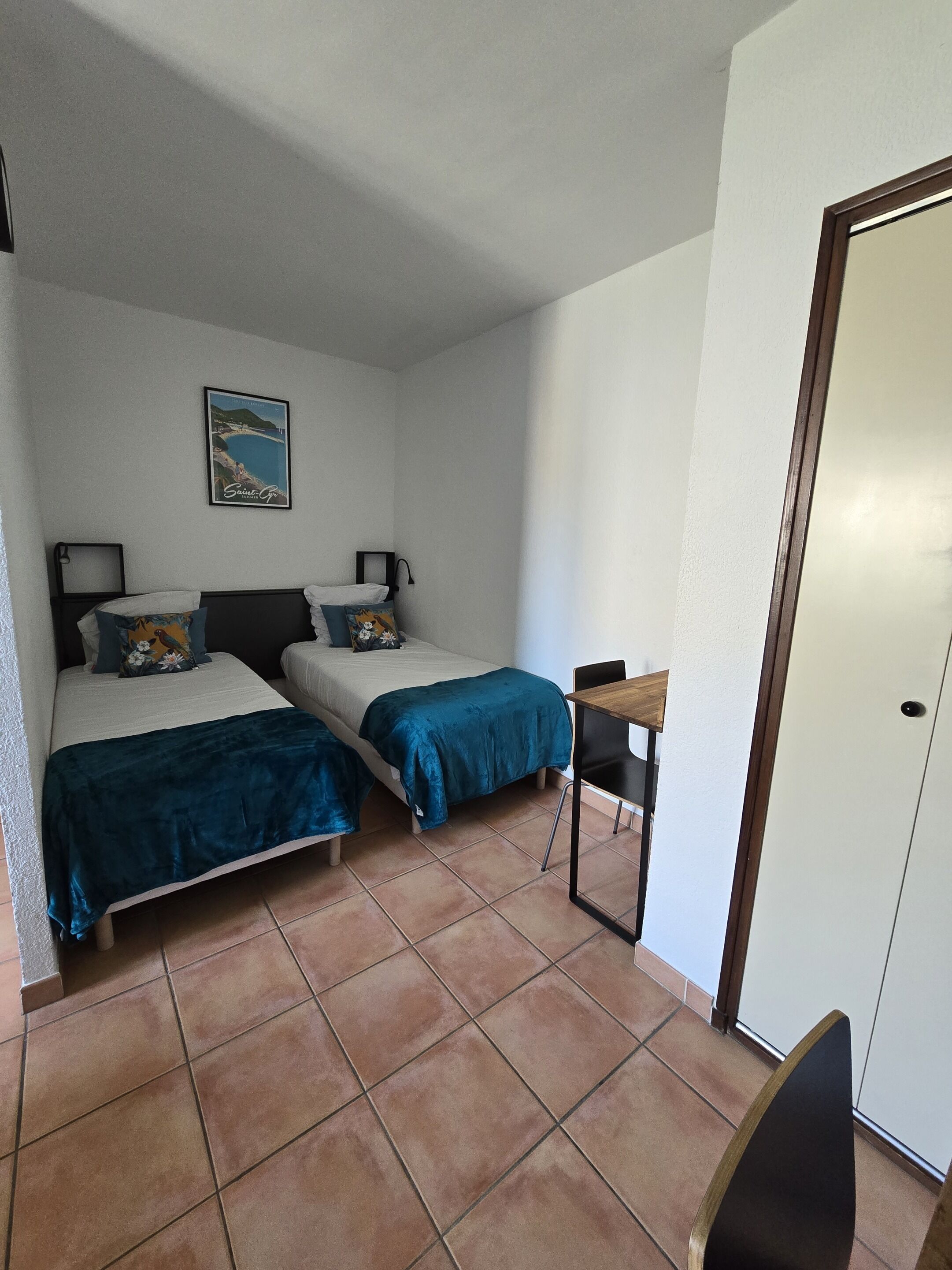 Un petit logement composé d’une seule pièce, comprenant deux lits, une petite table et une porte.