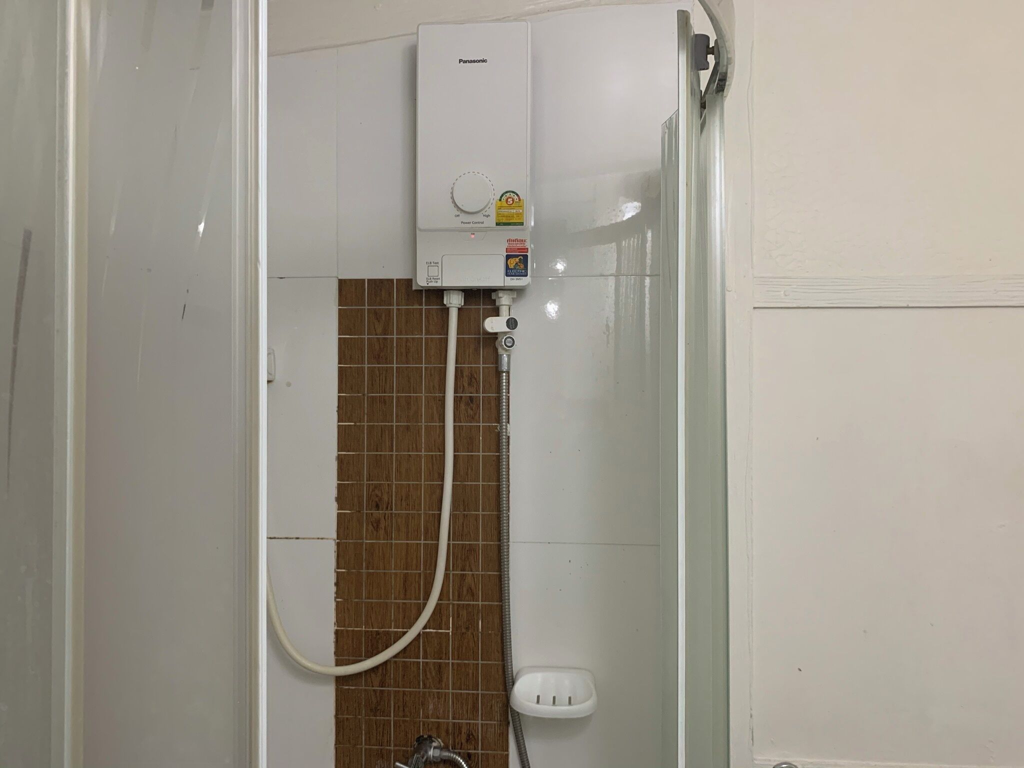 A bathroom with a white toilet, a shower with a brown tiled wall, and a white water heater on the wall.
