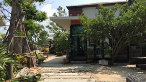 A pathway leading to a building with a modern design, surrounded by greenery and potted plants. - Rayonghouse Resort (Rayong)