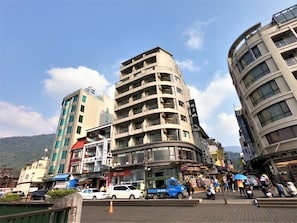 A multi-story building with balconies, a blue truck parked in front, and a busy street scene. - Ming Yue Hu Hotel (Yuchi)