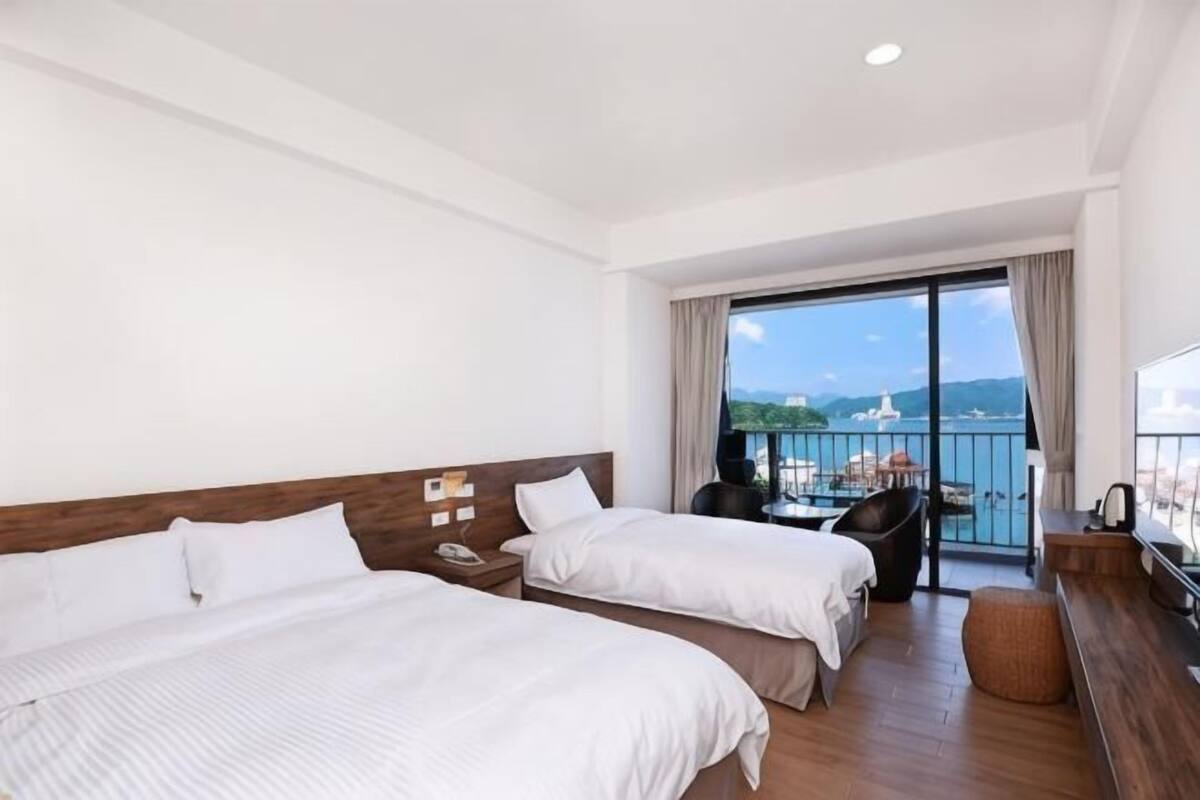 Une chambre d’hôtel avec deux lits, un bureau, une chaise et un balcon avec vue.