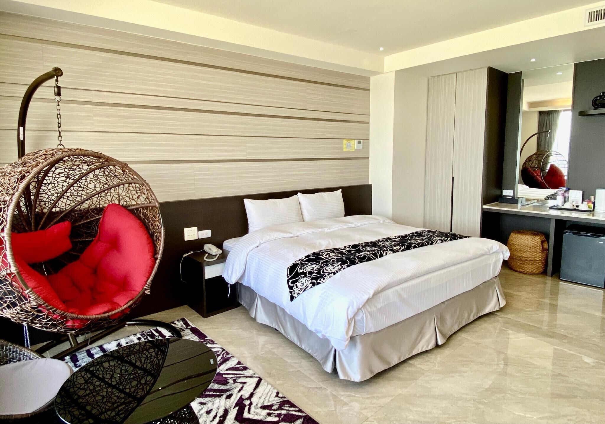 Ein modernes Hotelzimmer mit einem großen Bett, einem Hängekorbstuhl, einem Schreibtisch und einem Spiegel.