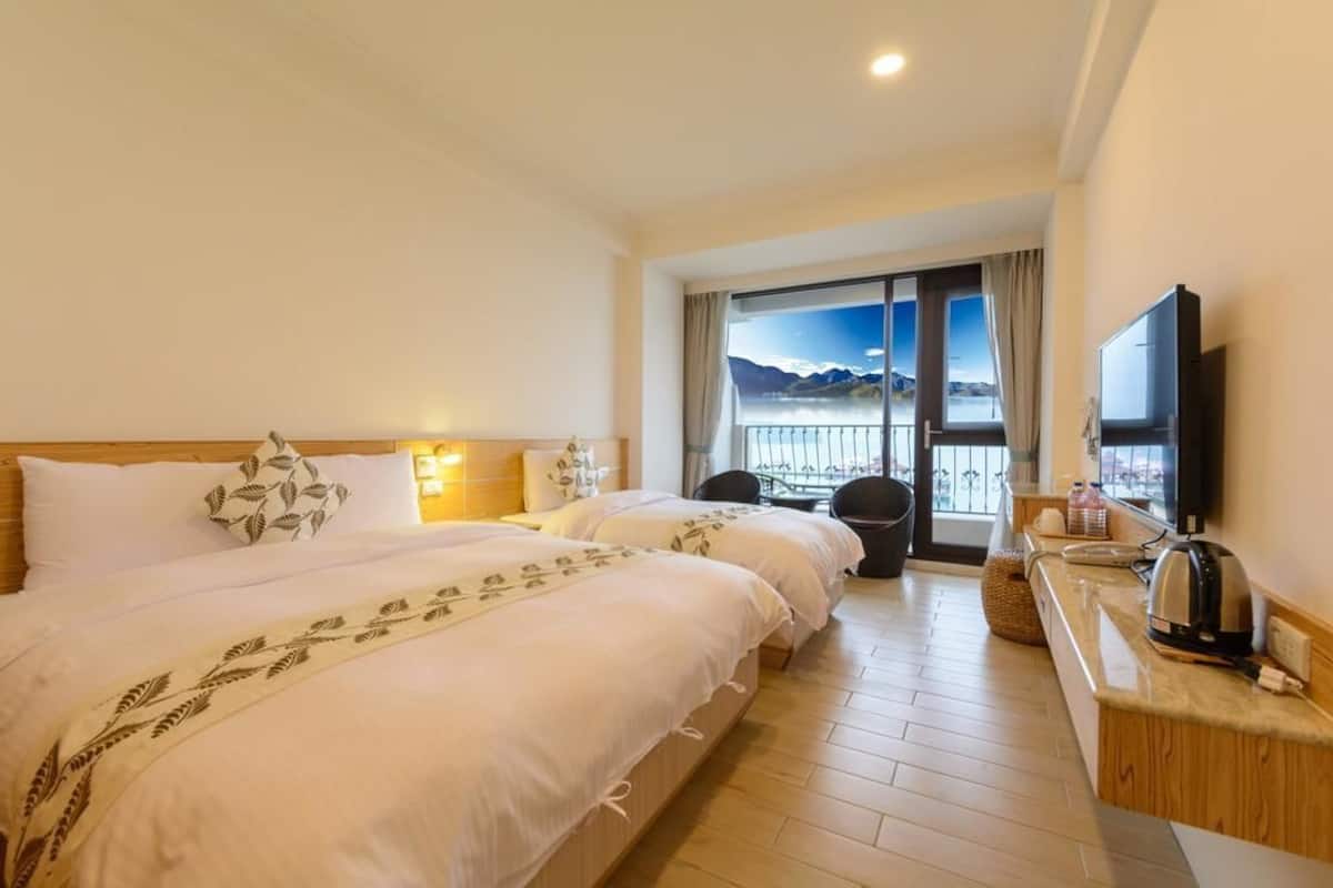 Une chambre d’hôtel avec deux lits, une télévision, une petite table avec une bouilloire, et une vue sur les montagnes par la fenêtre.