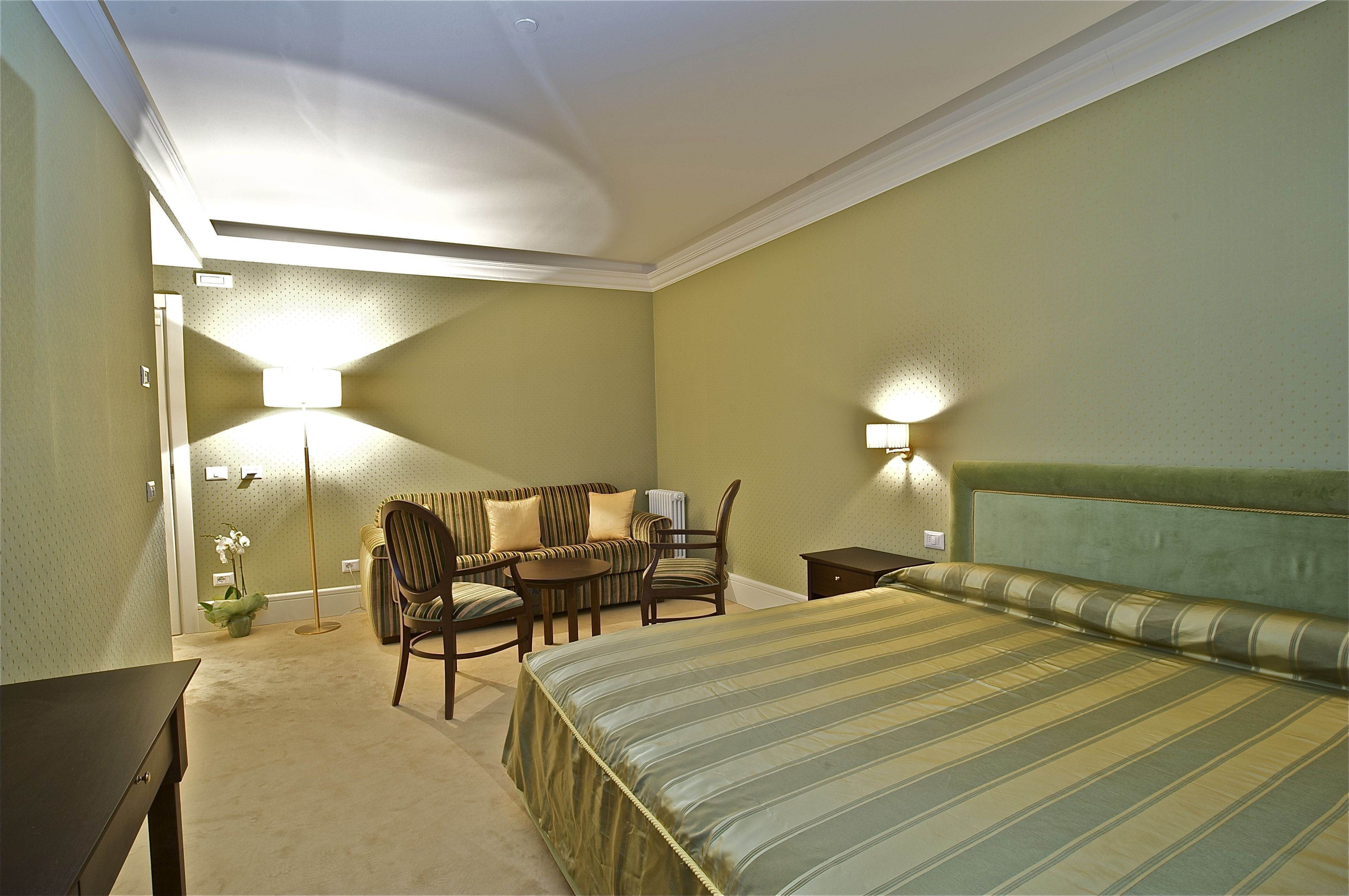 A hotel room with a bed, a desk, a chair, and a lamp.