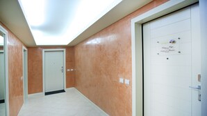 A hallway with a white door on the right, a closed door at the end, and a sign on the wall. - Design Suite Tirano (Tirano)