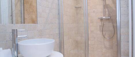 Un baño moderno con un lavabo grande de color blanco, una cabina de ducha con mampara de cristal y un mueble de tocador blanco.