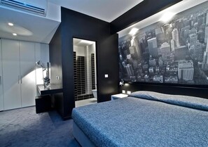 A modern bedroom with a large bed, a cityscape mural, a walk-in closet, and a bathroom with black tiles. - Design Suite Tirano (Tirano)