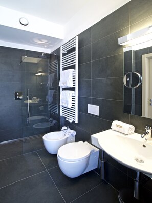 Een moderne badkamer met een douchecabine, twee toiletten, een wastafel en een spiegel.